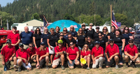 A large group of 28 people posed outdoors, with a mountainous backdrop and two American flags.